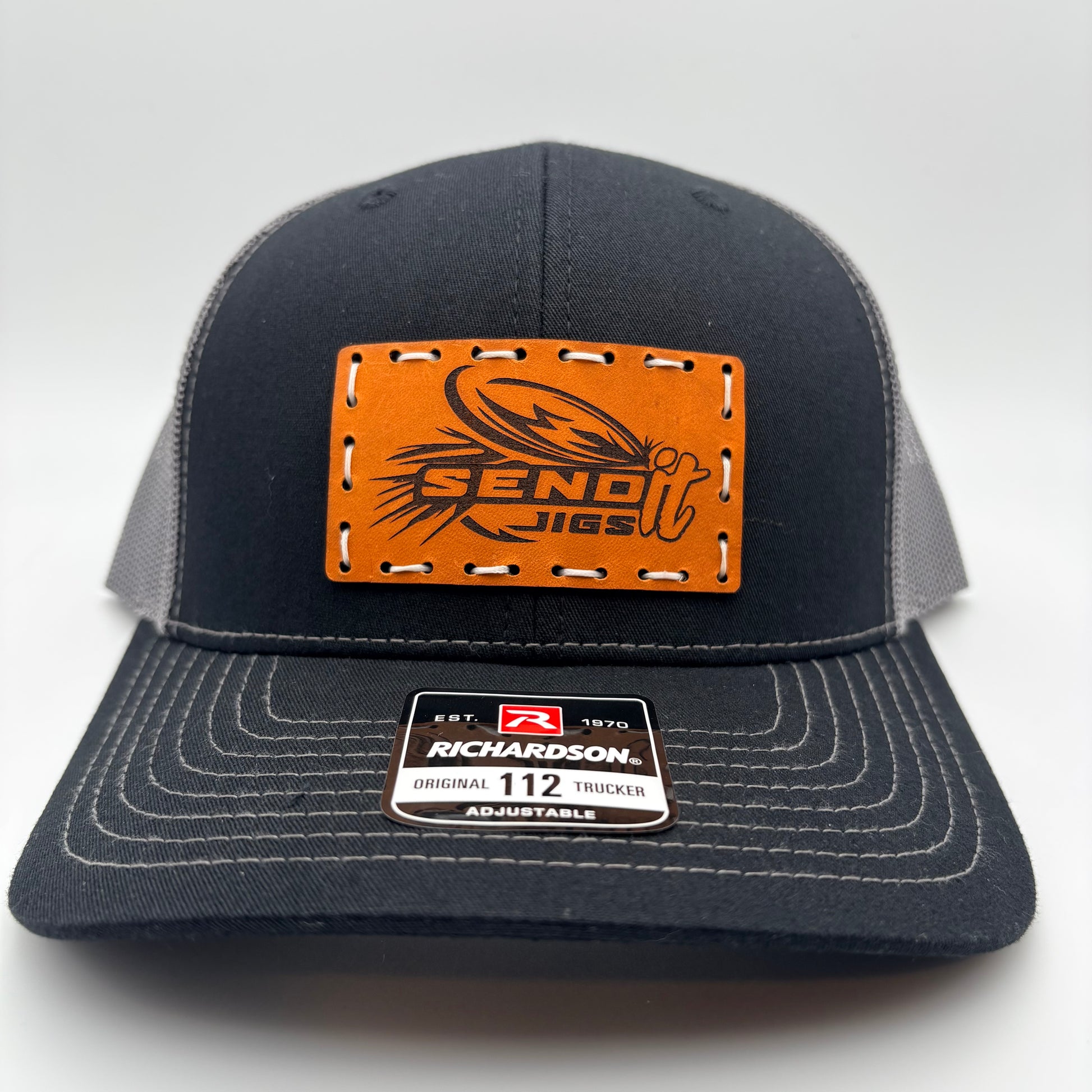 Black and gray trucker cap with leather patch and Richardson logo on a white background